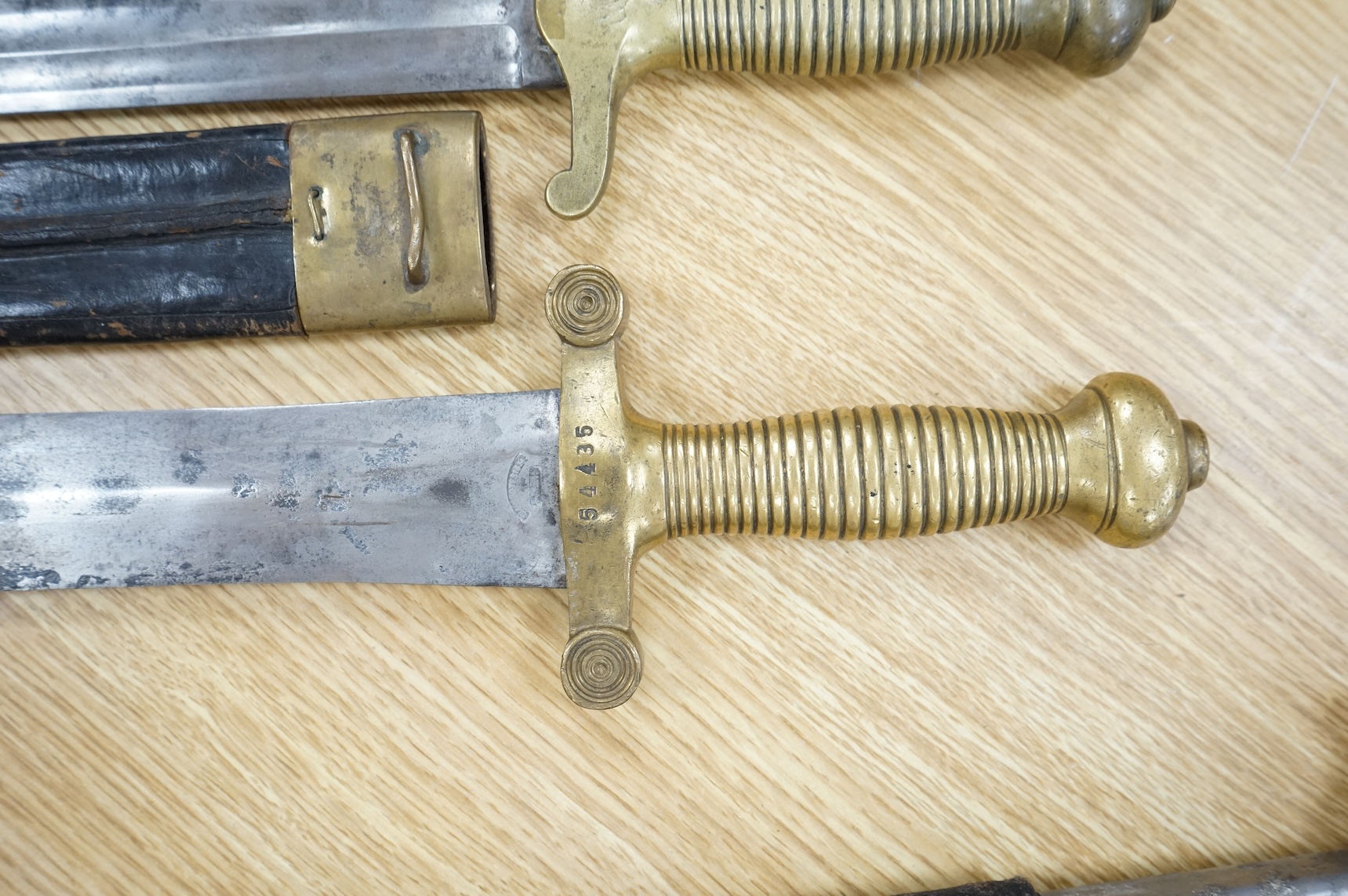 Three Continental infantry officer’s sidearms briquette, the first stamped Paris, in its brass mounted leather scabbard, another similar with sawback blade (illegible stamp), and another similar with thin blade, stamped